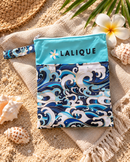 Lalique Ocean Wave pouch on a beach towel beside sand and shells