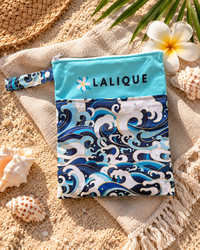 Lalique Ocean Wave pouch on a beach towel beside sand and shells